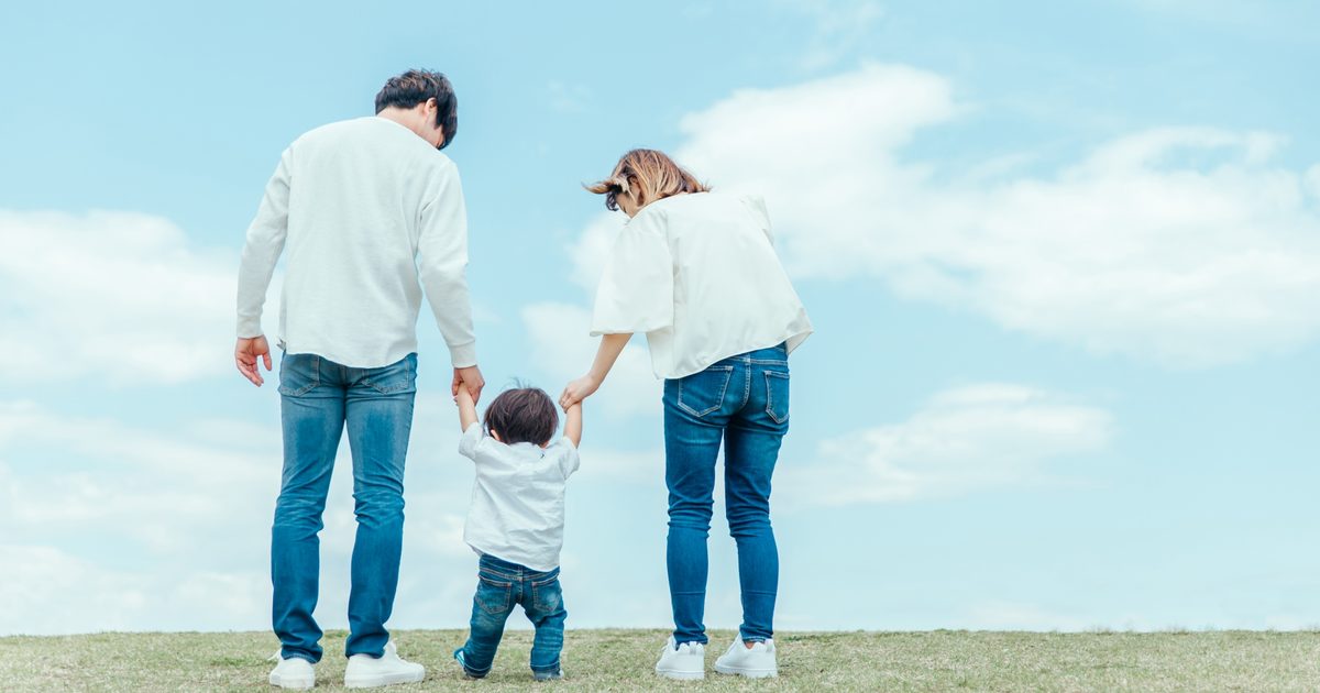 青空の下で手をつなぐ親子の後ろ姿
