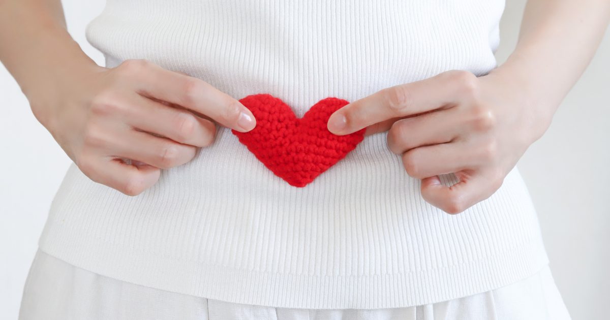 お腹の前で赤いハートを持つ妊婦さんの手